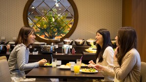 A dining area with a round table, chairs, and a large window with a view of greenery. - Hiyori Hotel Maihama (Urayasu)