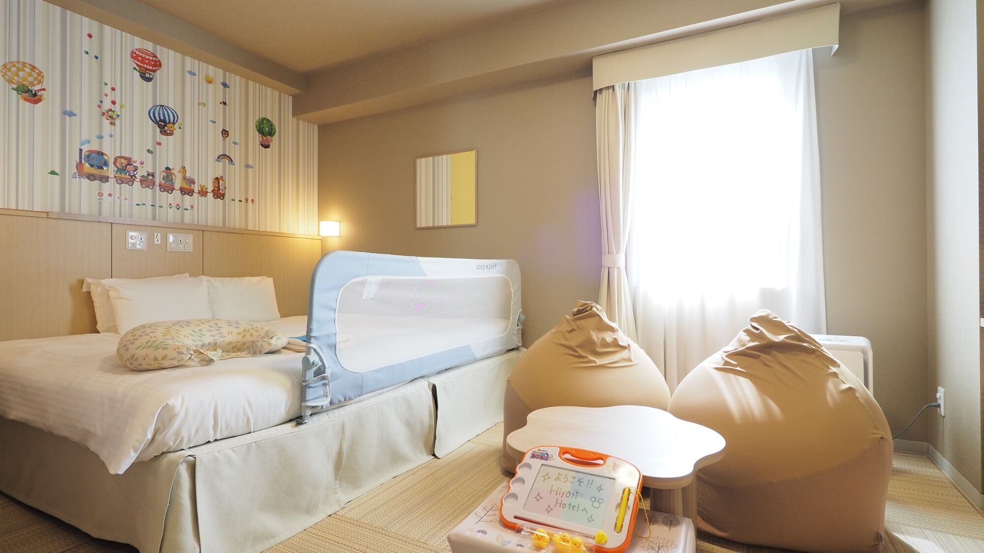 A hotel room with a bed, a desk, a bean bag, and a window with curtains.