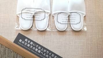 A pair of white slippers with instructions in both English and Japanese, placed on a textured fabric background.