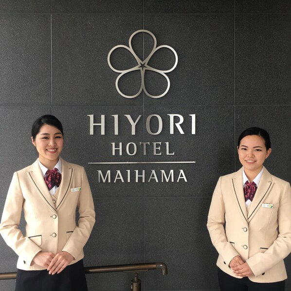 Two staff members in front of a sign for Hiyori Hotel Maihama.
