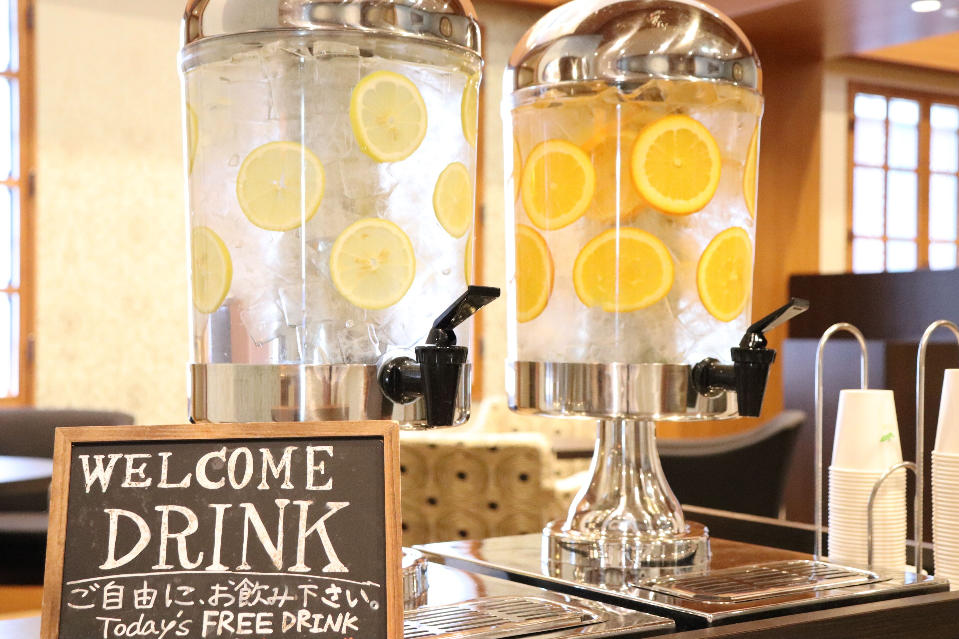 Two large dispensers with ice and lemon slices, a sign offering a free drink, and a coffee machine.