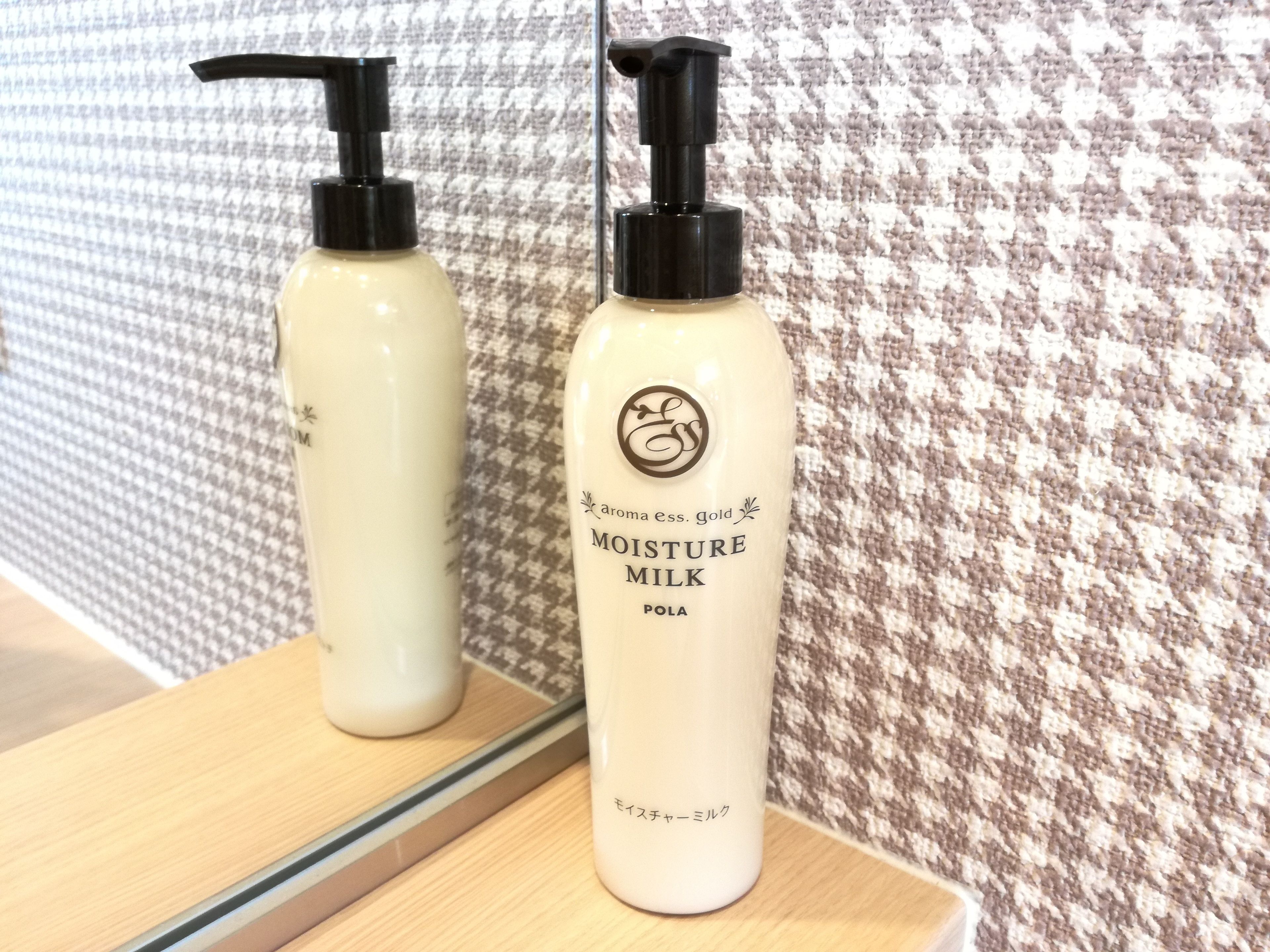 Two bottles of Moisture Milk on a wooden surface with a mirror reflecting them.