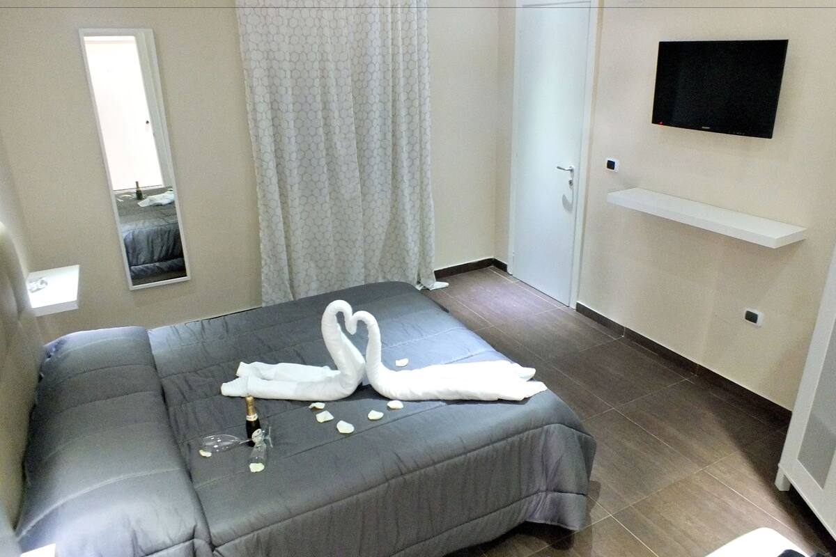 A bedroom with a bed, a TV, a mirror, and a door.