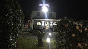 Een hotel met een opvallend 'HOTEL' bord, een goed verlichte entree en een kleine tuin met een palmboom.