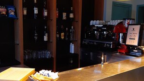 A bar area with a counter, bottles of liquor, a coffee machine, and a bowl of snacks. - Hotel Alabama (Rimini)