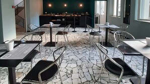 A modern dining area with stone-tiled flooring, metal chairs, and tables. There are overhead lights and a visible exit sign. - Hotel Alabama (Rimini)