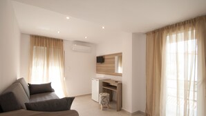 A modern, well-lit room with a sofa, a small desk, and a television. - Pension Avocado (Skiathos)