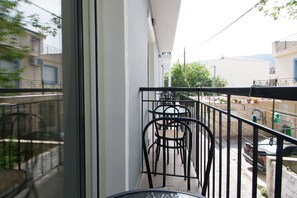 A balcony with a railing, a row of chairs, and a view of the street and buildings in the background. - Pension Avocado (Skiathos)