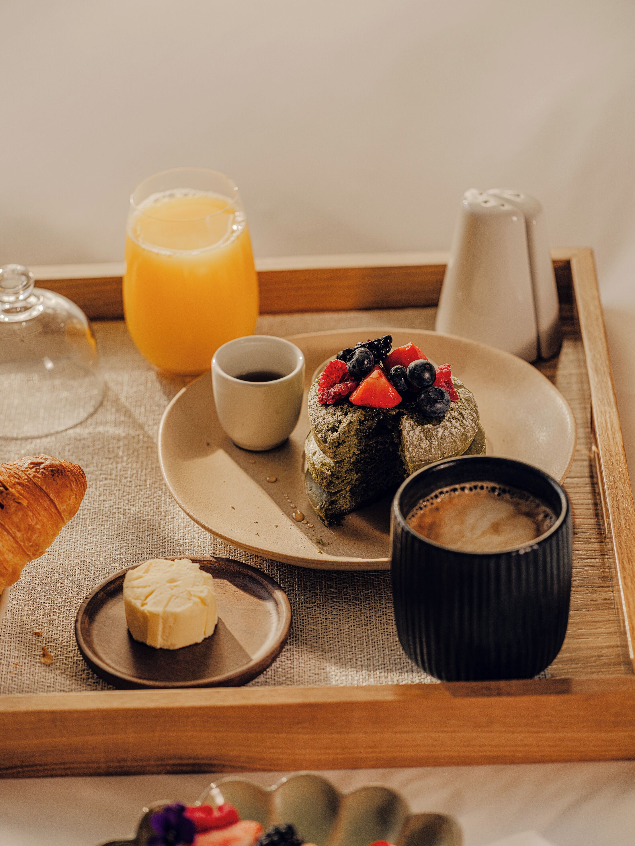A breakfast tray with croissant, butter, coffee, a pastry topped with berries, and a glass of orange juice.