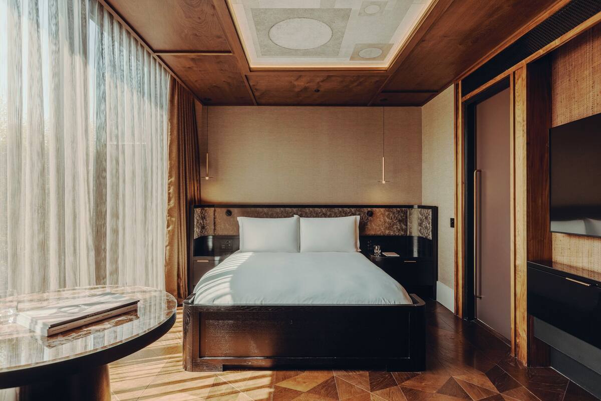 A modern hotel room with a skylight, a bed with white linens, a round table, and a TV.