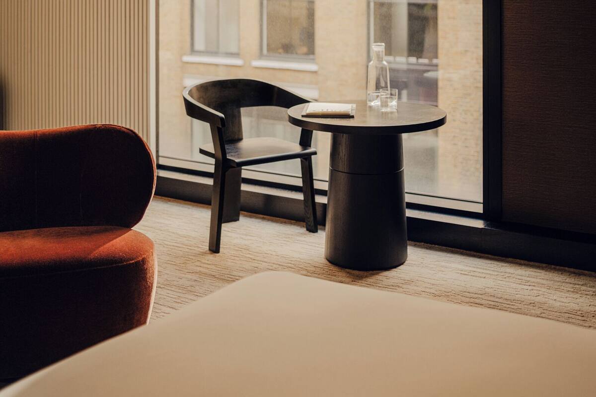 A hotel room with a large window, a round table with a glass, a chair, and a bed.