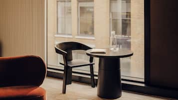A hotel room with a large window, a round table with a glass, a chair, and a bed.