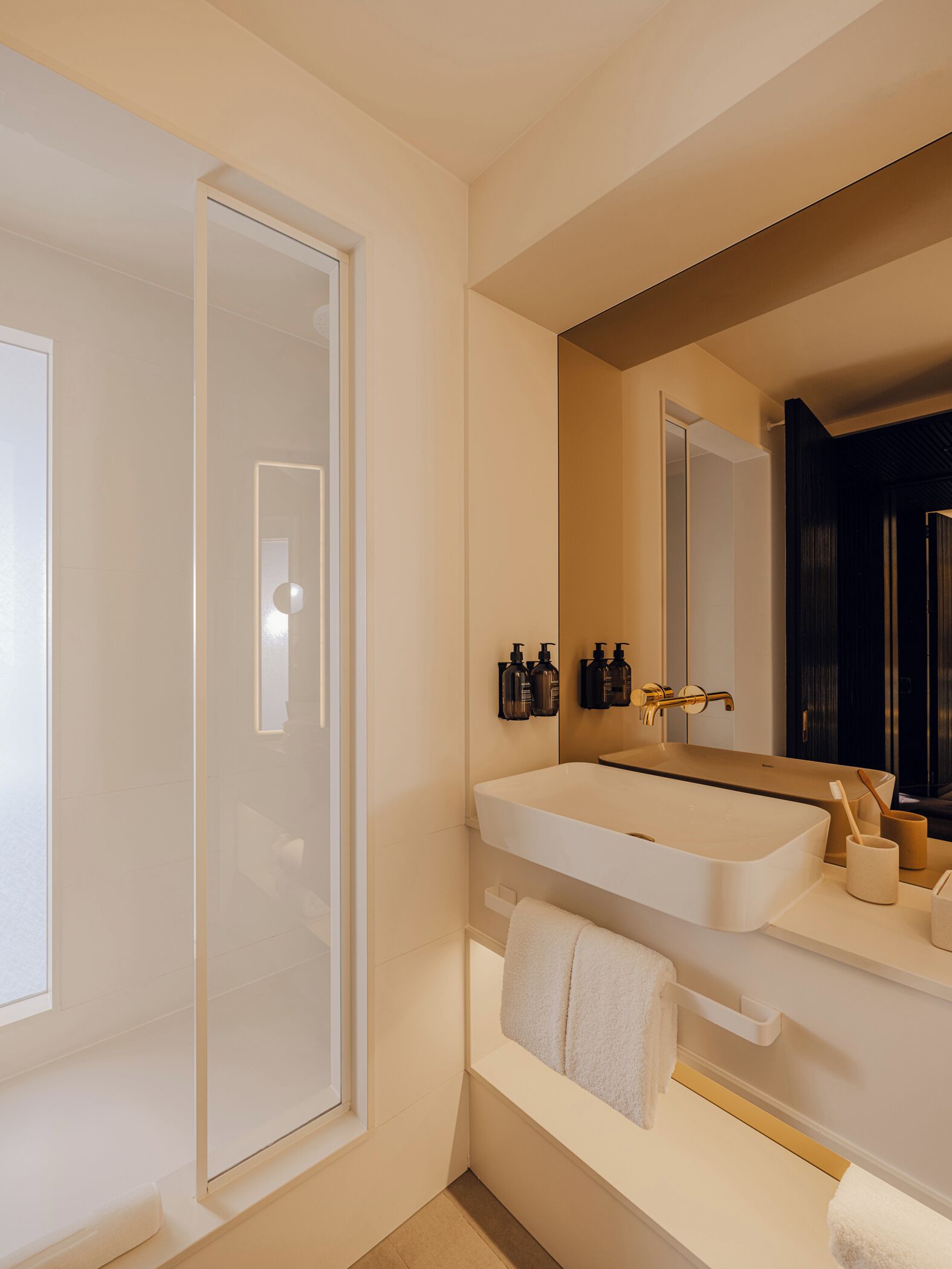 Un baño moderno con un espejo grande, un lavabo blanco y una zona de ducha.