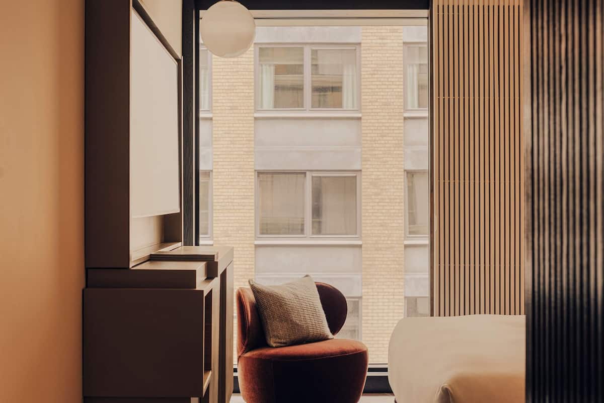 A modern bedroom with a bed, a chair, a desk, and a large window.