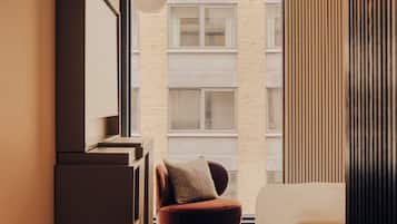 A modern bedroom with a bed, a chair, a desk, and a large window.