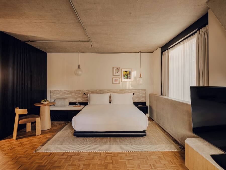 Una habitación de hotel moderna con una cama grande, un televisor, una mesita con un frutero y una silla.