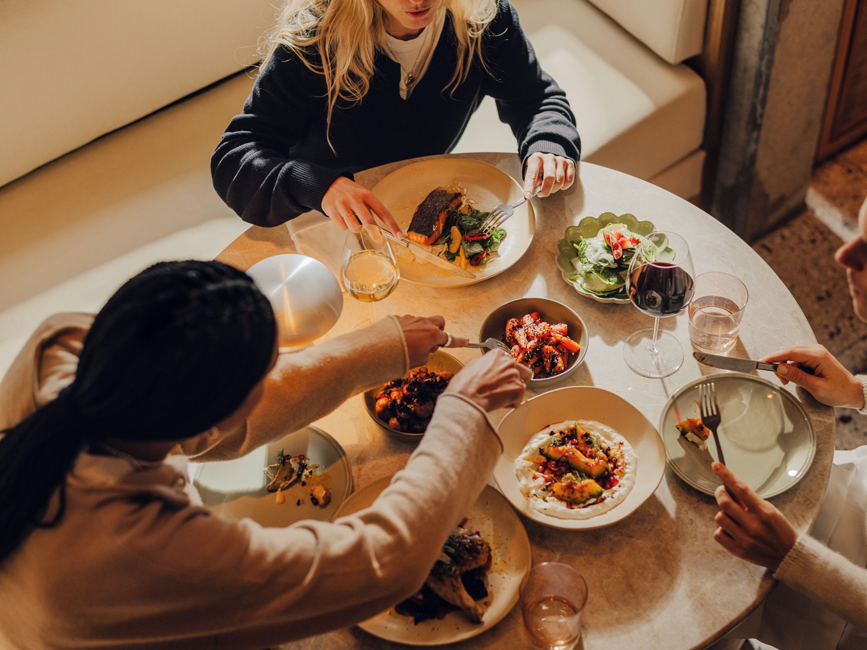 A group of people dining at a round table with various dishes and glasses of wine.