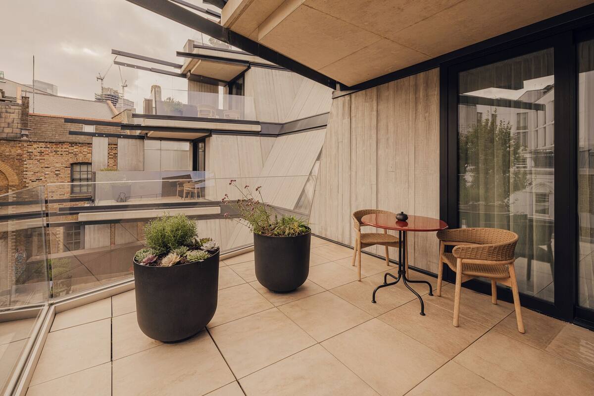 A modern balcony with potted plants, a wicker chair, and a small table.