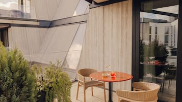 A modern outdoor patio with a round table and wicker chairs, surrounded by potted plants.