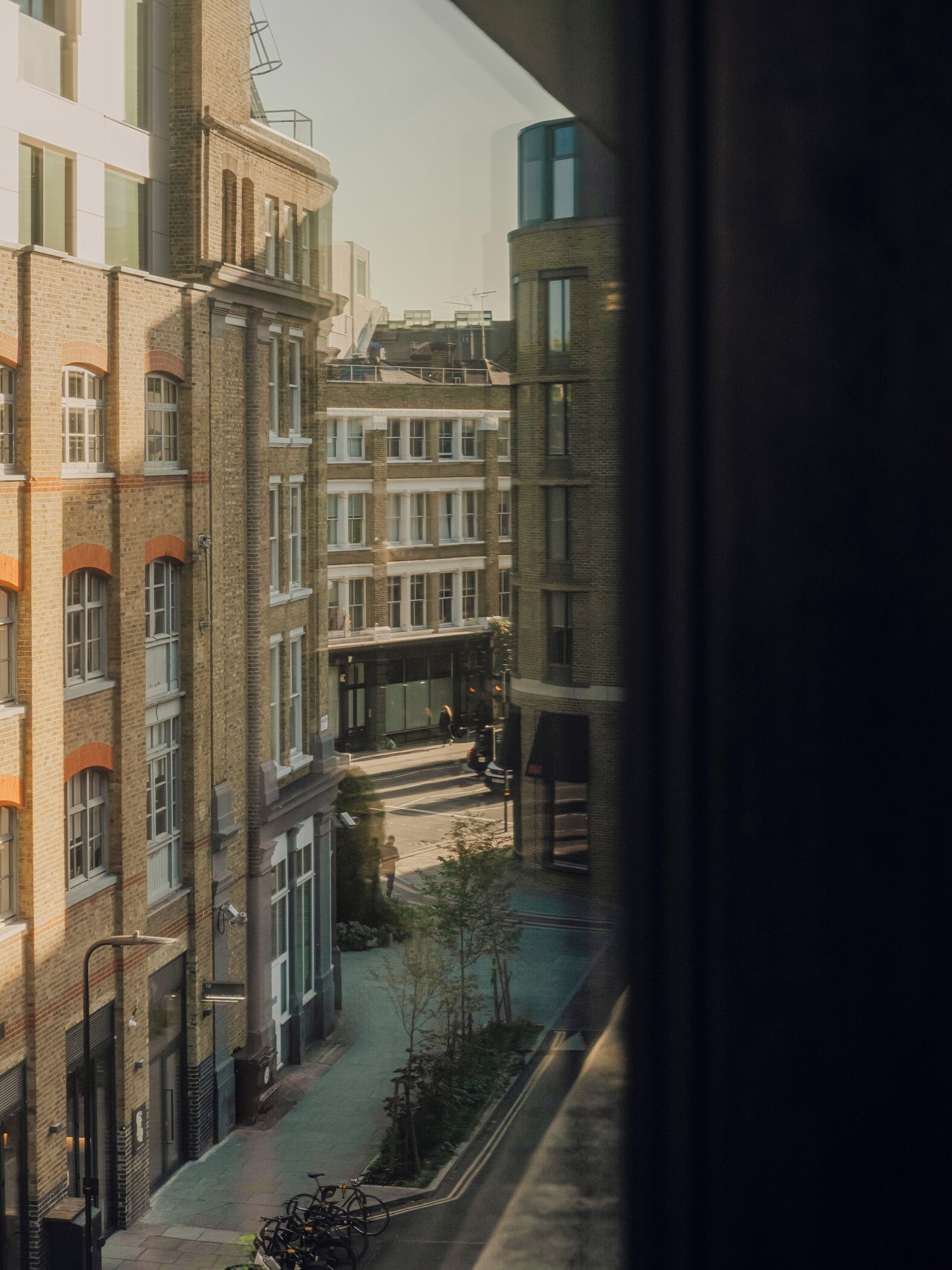 A multi-story urban building with a mix of brick and glass facades, a visible street with pedestrians, and a bicycle parked outside.