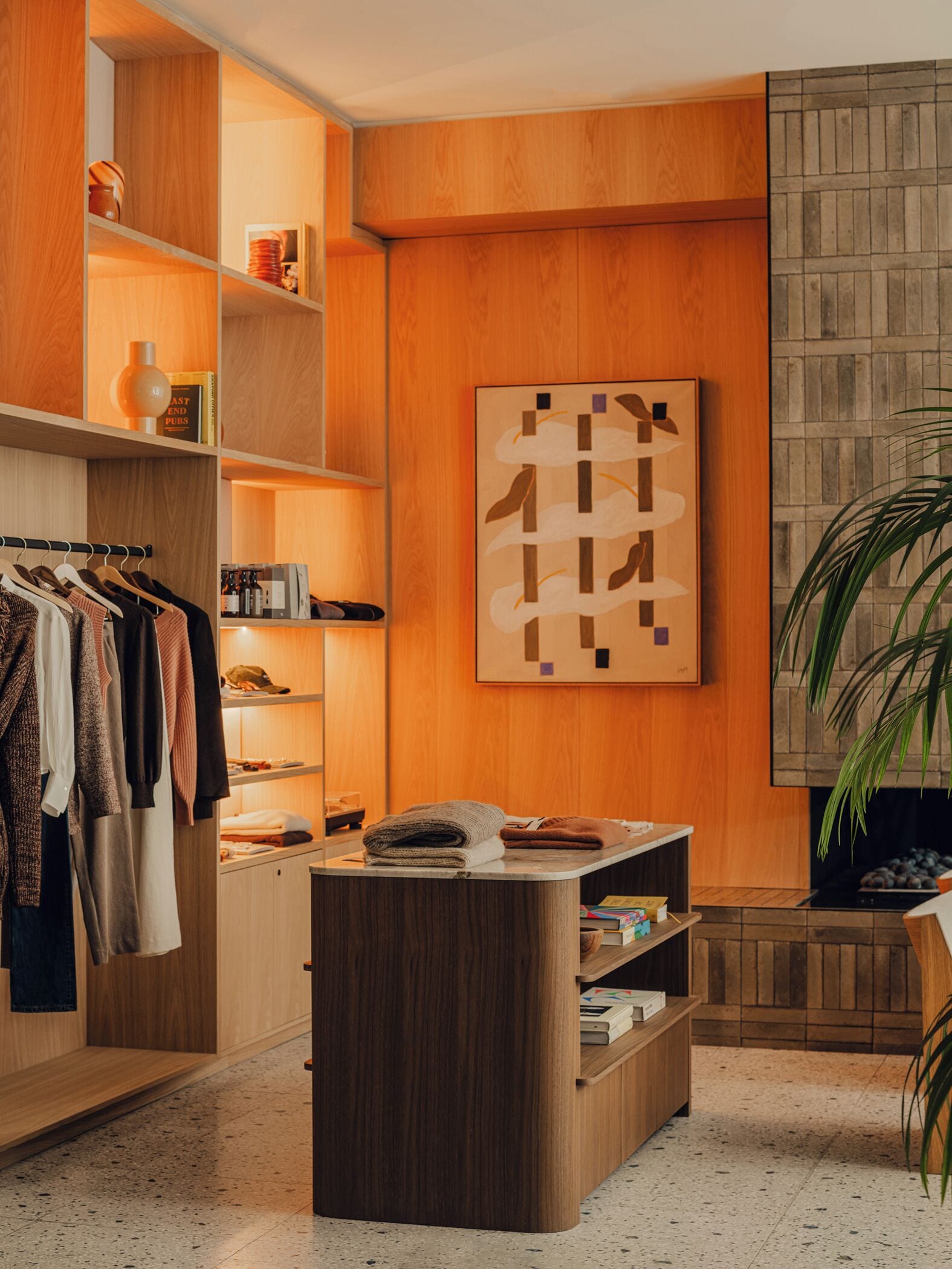 A modern room with wooden shelving, a clothing rack, a small table with books, and a large abstract painting on the wall.