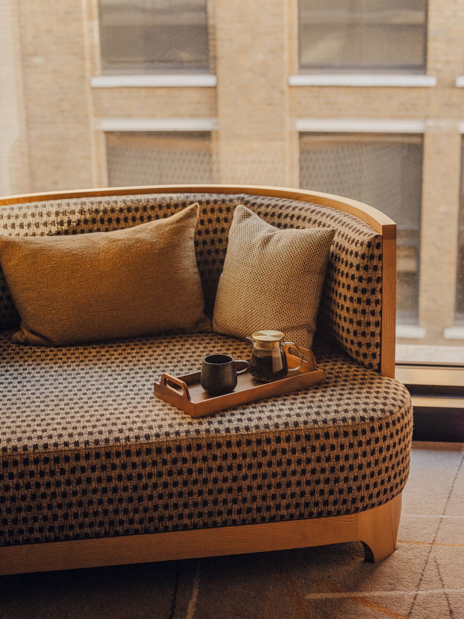 Un canapé confortable, orné de motifs, avec une structure en bois, accompagné de deux coussins et d’un plateau sur lequel se trouvent une théière et une tasse.
