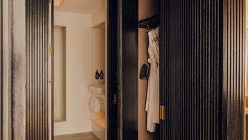 A hallway with a wooden floor leading to a bathroom with a towel rack and a sink.