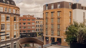 Un balcón con mobiliario de mimbre, una planta en maceta y vistas de edificios circundantes.