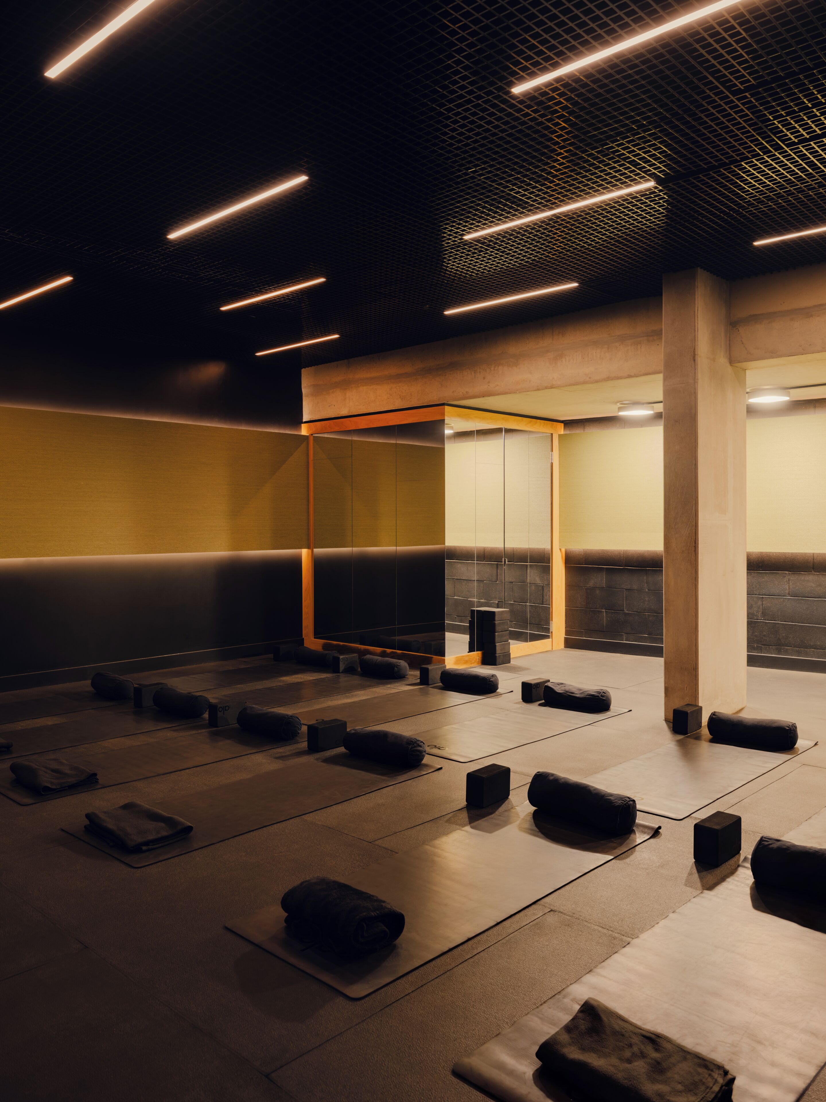 A modern, dimly lit room with a geometric ceiling design, wooden accents, and a mirrored wall.