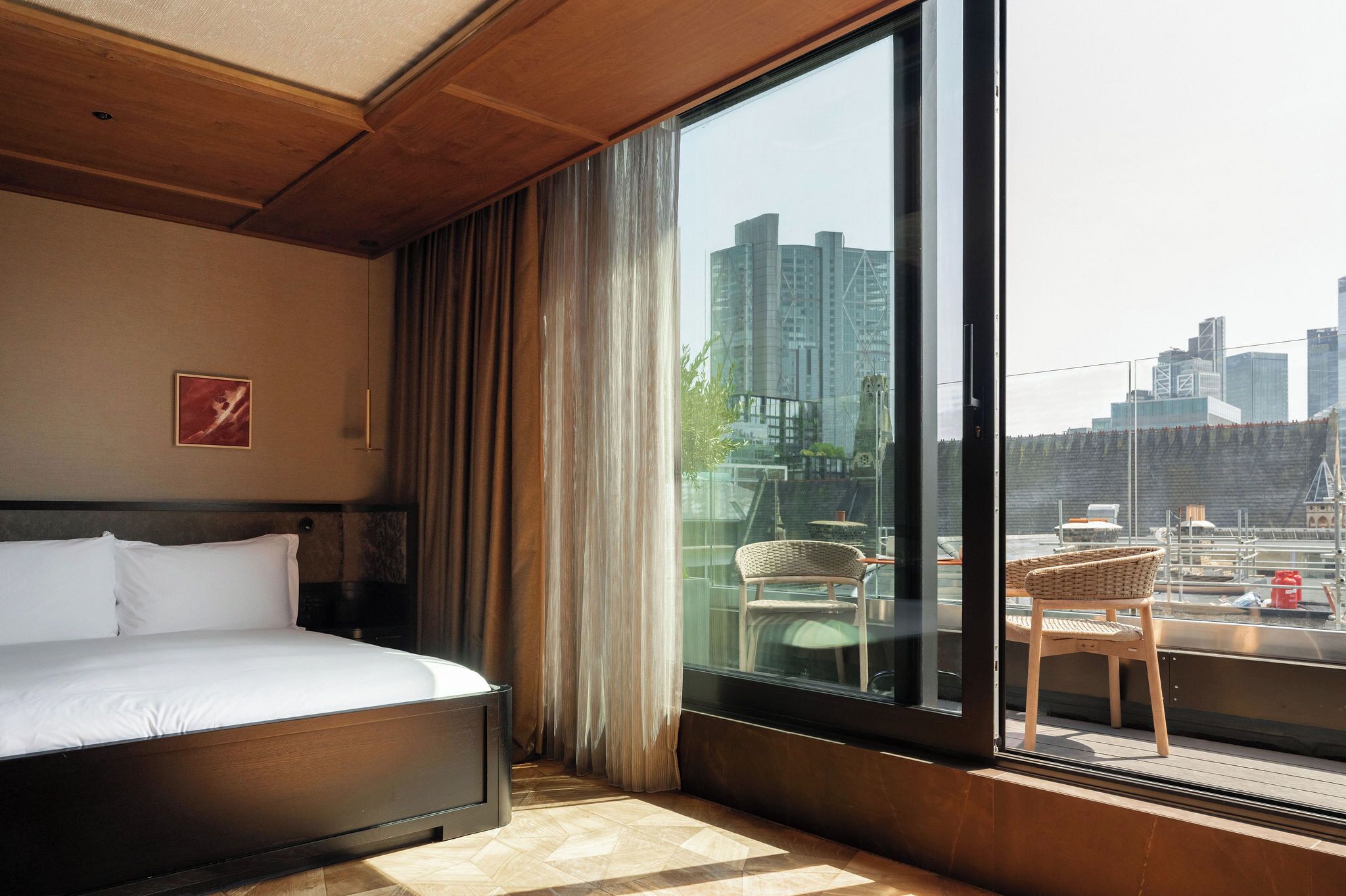 A hotel room with a large bed, a view of the city through a window, and a chair by the window.