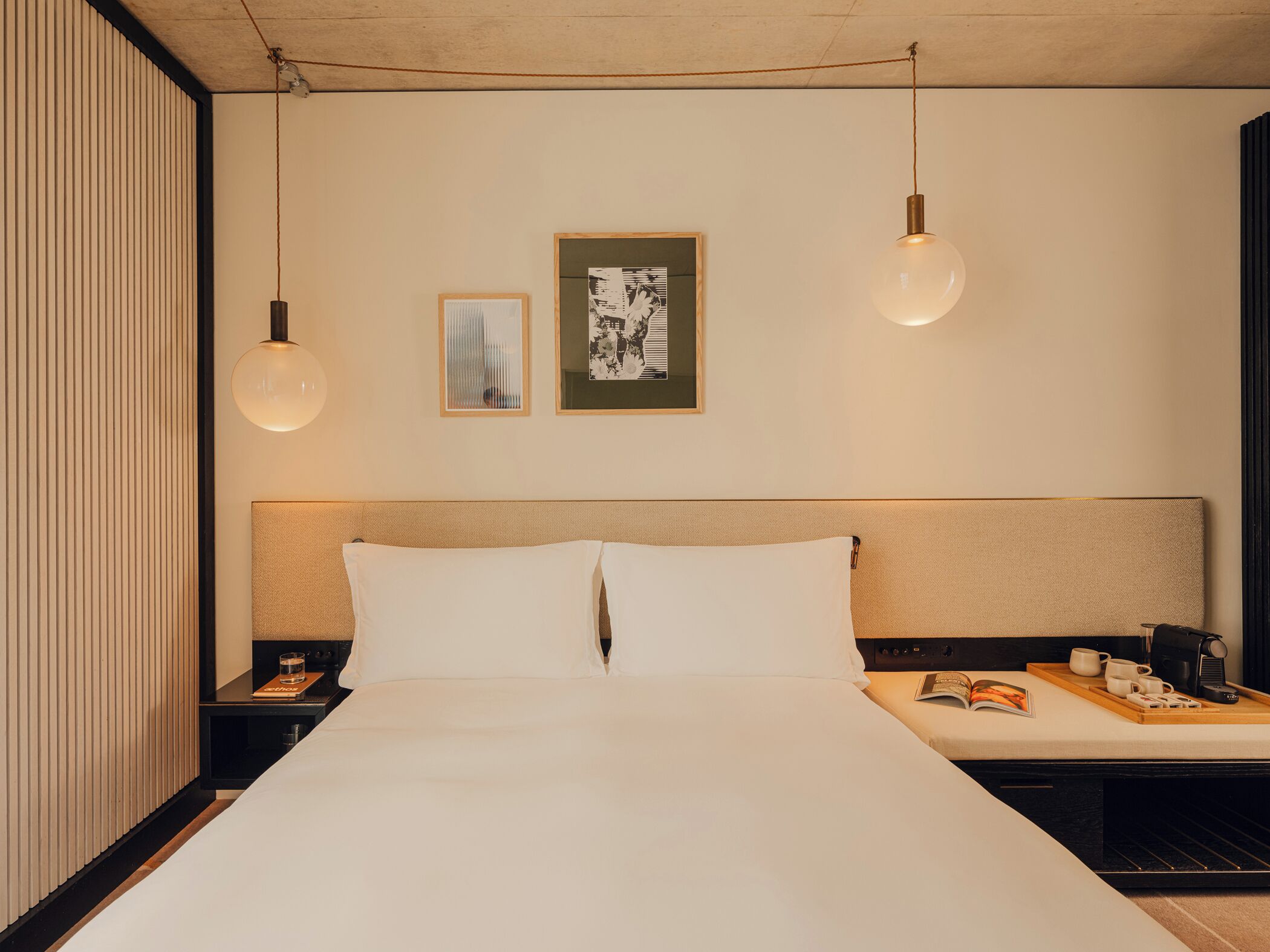 A hotel room with a large bed, bedside tables, a nightstand, a reading light, a framed picture, and a wall-mounted shelf.