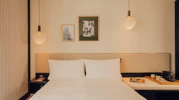 A hotel room with a large bed, bedside tables, a nightstand, a reading light, a framed picture, and a wall-mounted shelf.