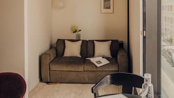 Un espacio habitable compacto con un sofá, una mesita con vasos y una silla roja.