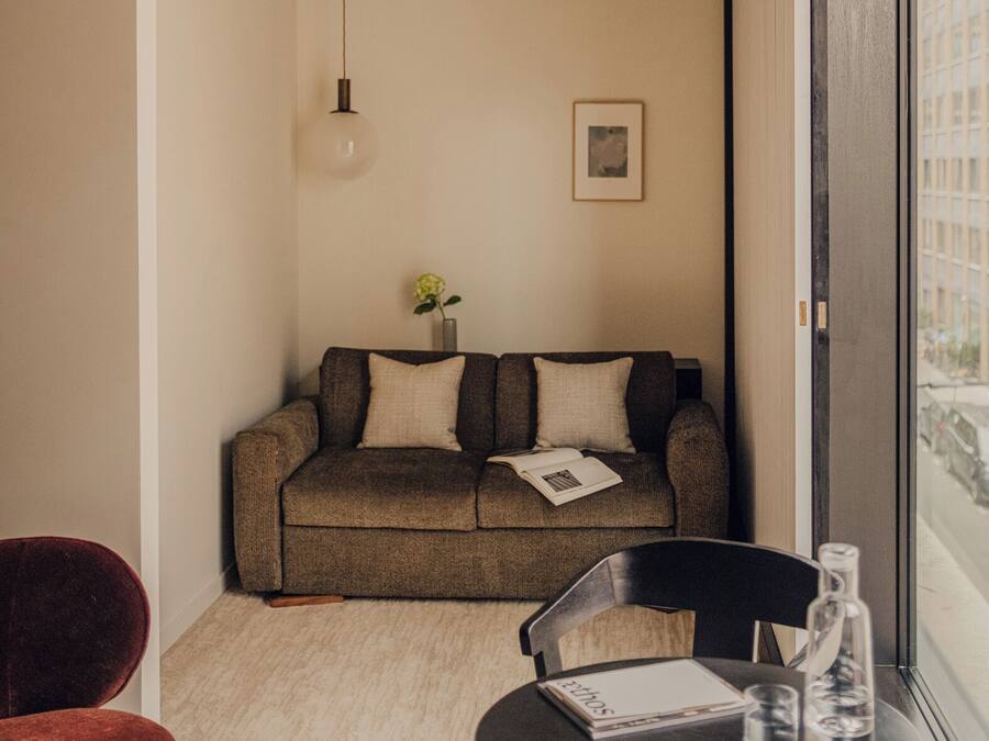 A compact living space with a sofa, a small table with glasses, and a red chair.