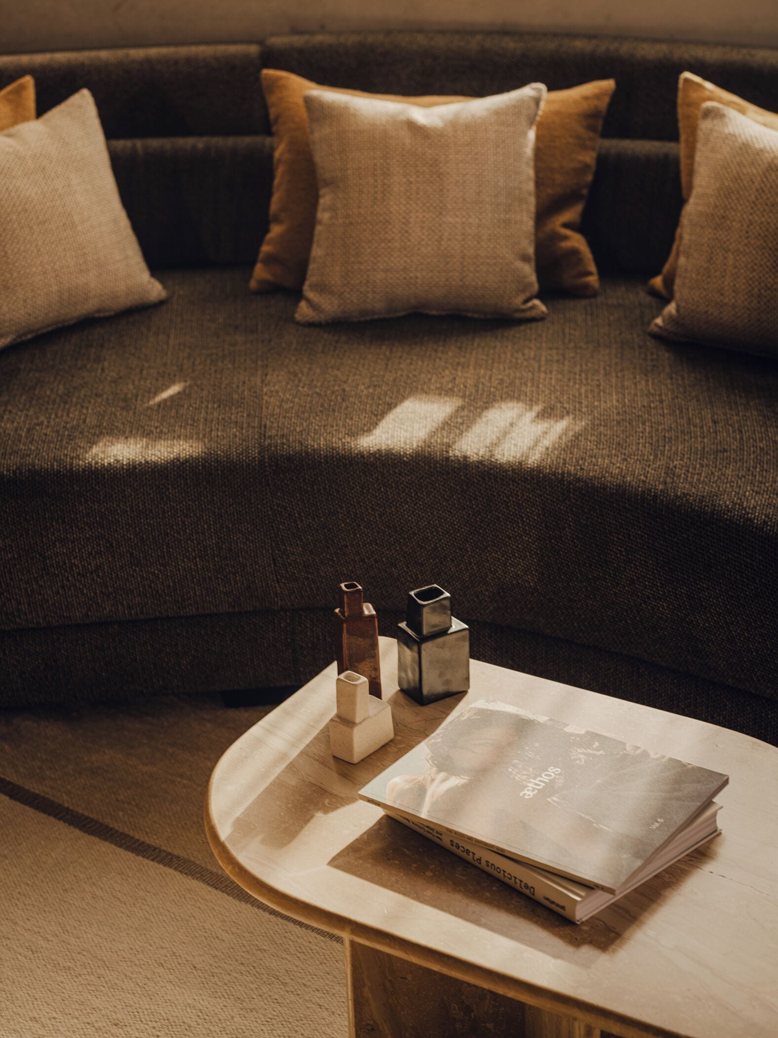 A dark brown sofa with three beige cushions, a small wooden table with a stack of books, and three geometric decorative objects.
