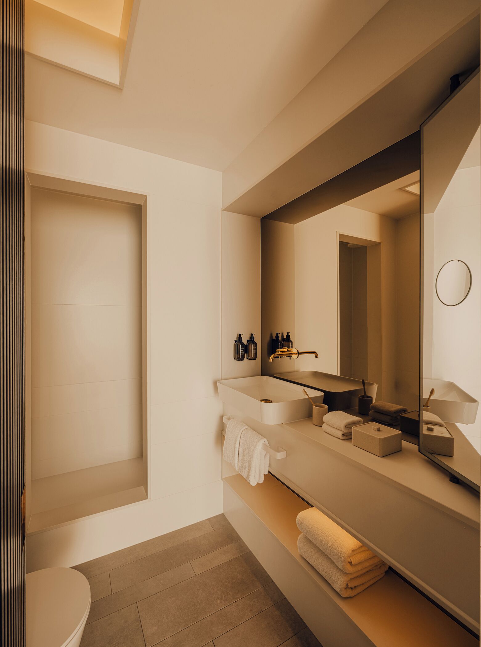 A modern bathroom with a large mirror, a bathtub, a toilet, and a vanity with a sink and toiletries.