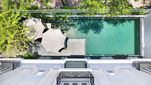 A modern outdoor pool area with a large, green pool, white steps leading down to the pool, and a white railing surrounding the pool. - Hoi An Canal House Riverside By Haviland (Da Nang)