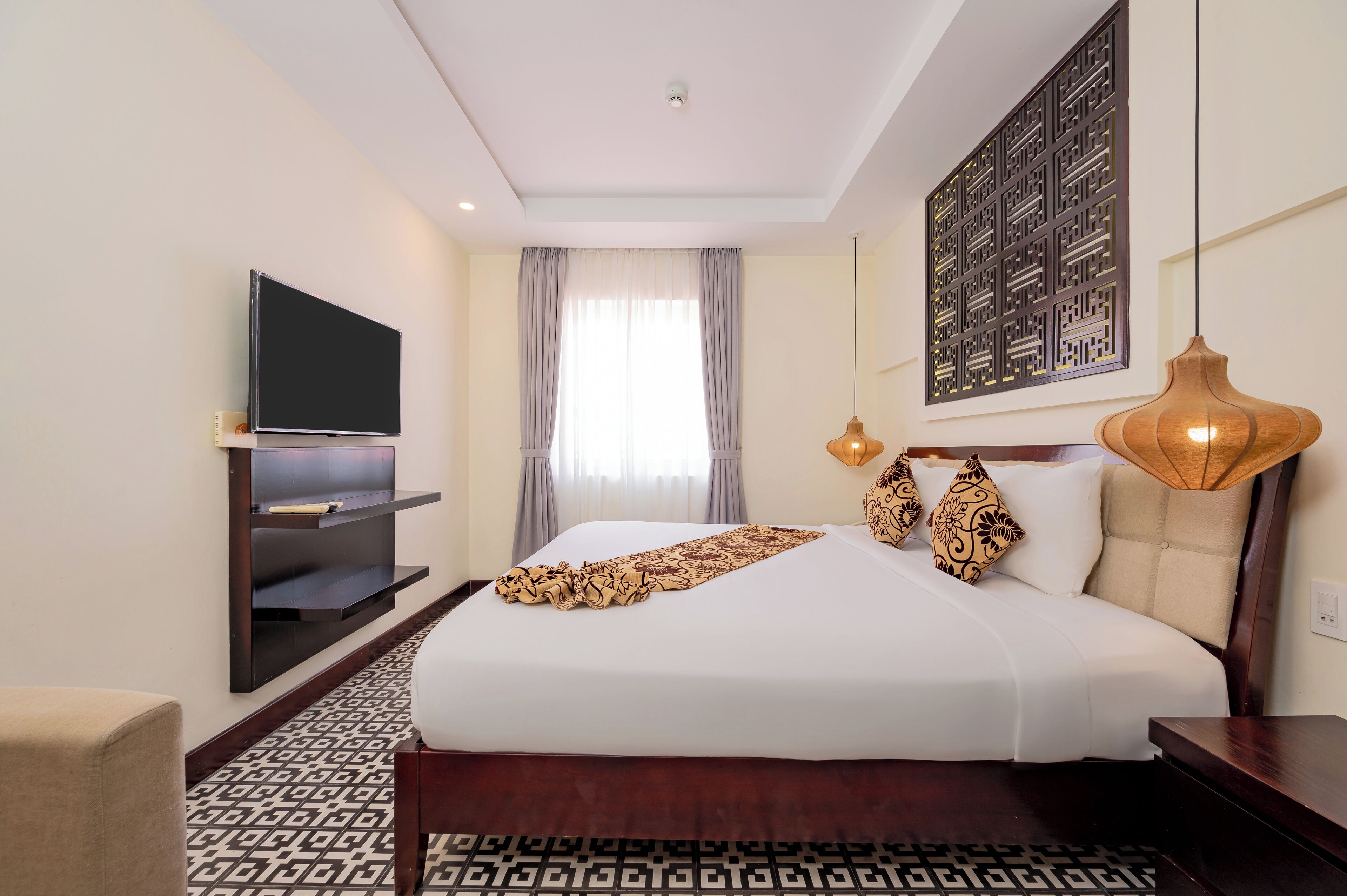 A hotel room with a large bed, a flat-screen TV mounted on the wall, a decorative wall panel, and a patterned rug.