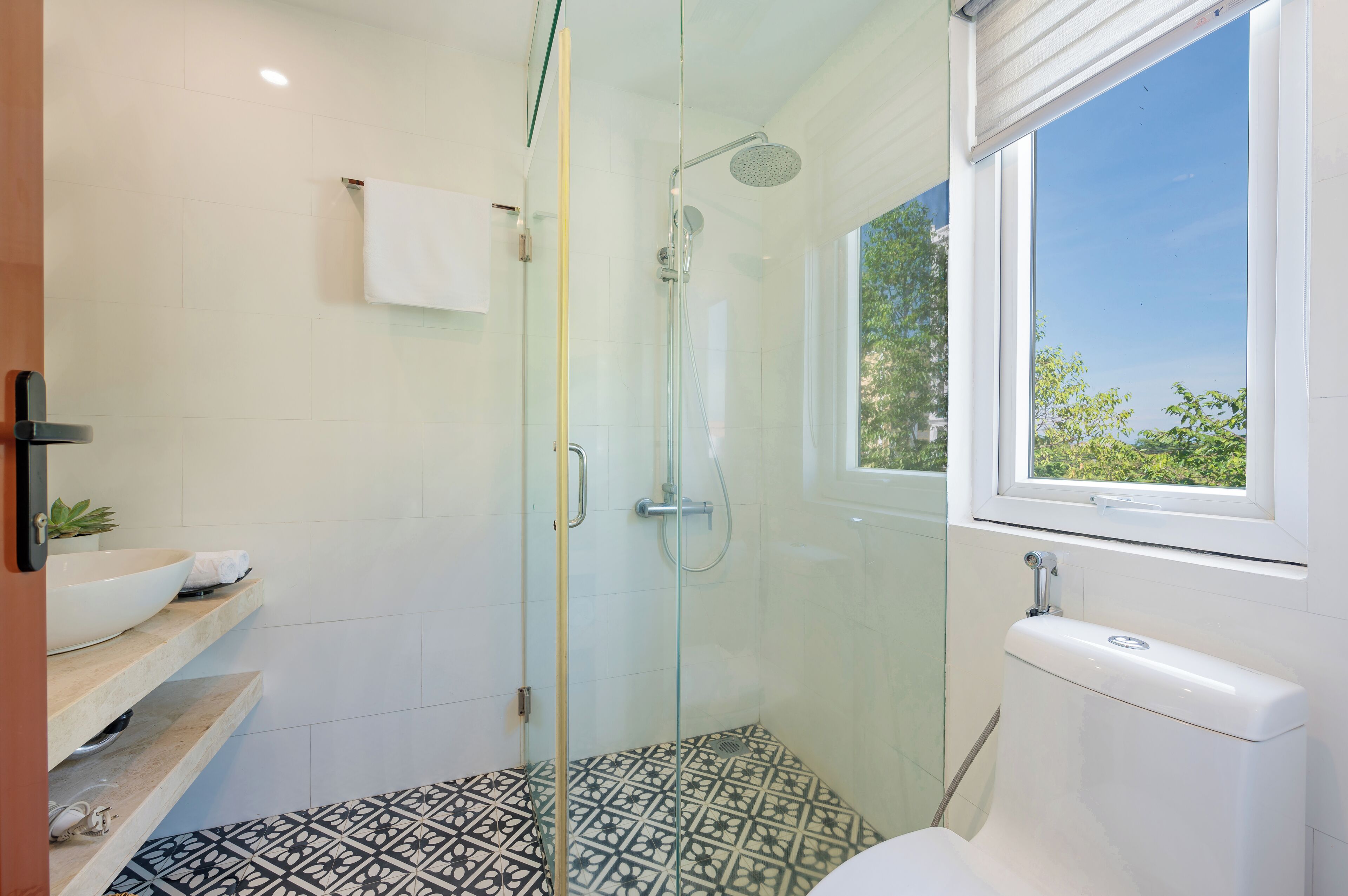 Een moderne badkamer met een douchecabine van glas, een wit toilet en een raam met uitzicht op groen.