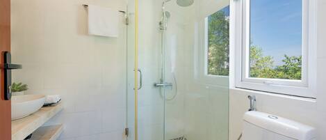 A modern bathroom with a glass-enclosed shower, a white toilet, and a window with a view of greenery.