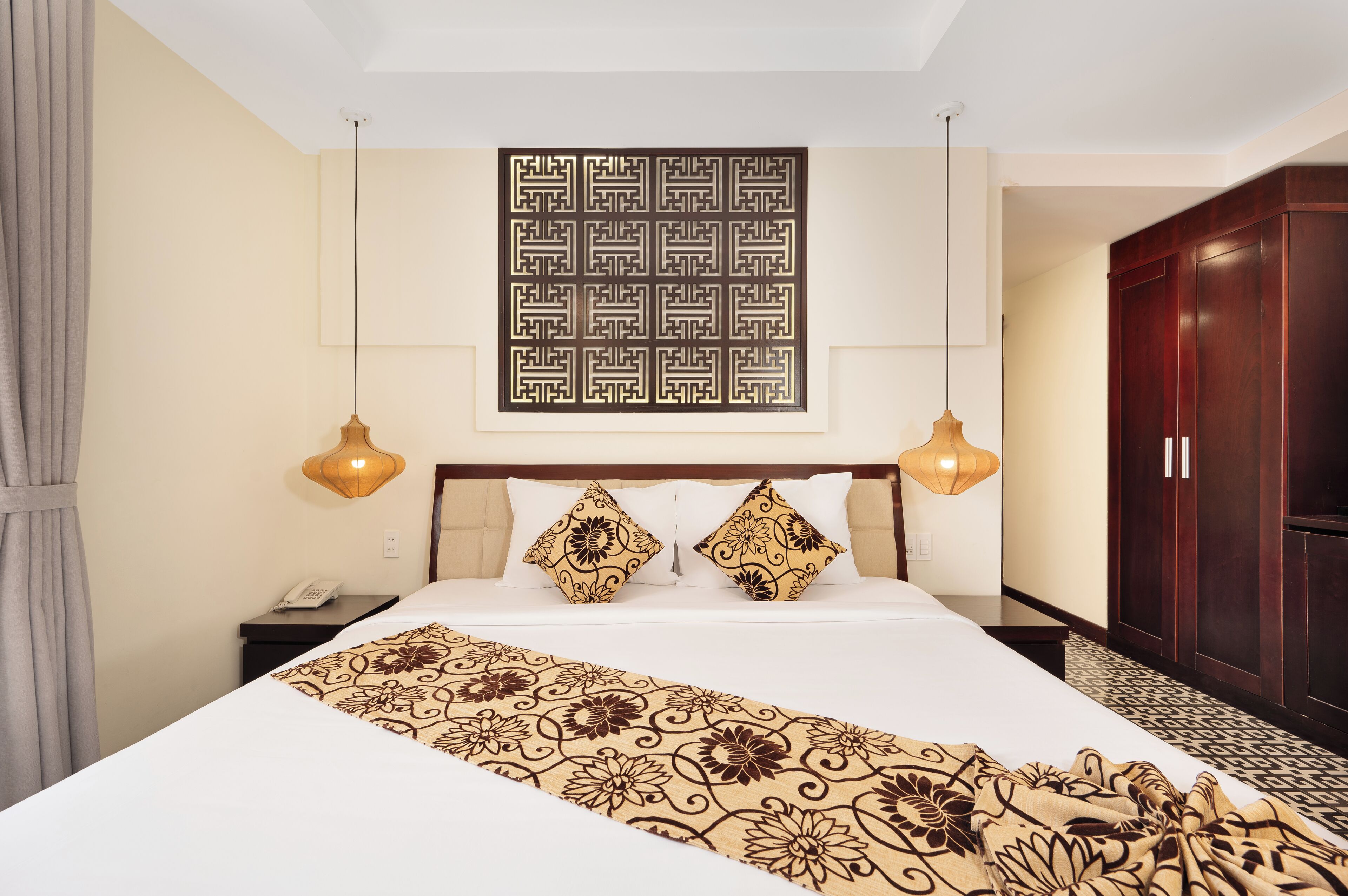 A hotel room with a large bed, two bedside lamps, a telephone, a wardrobe, and a decorative wall panel.