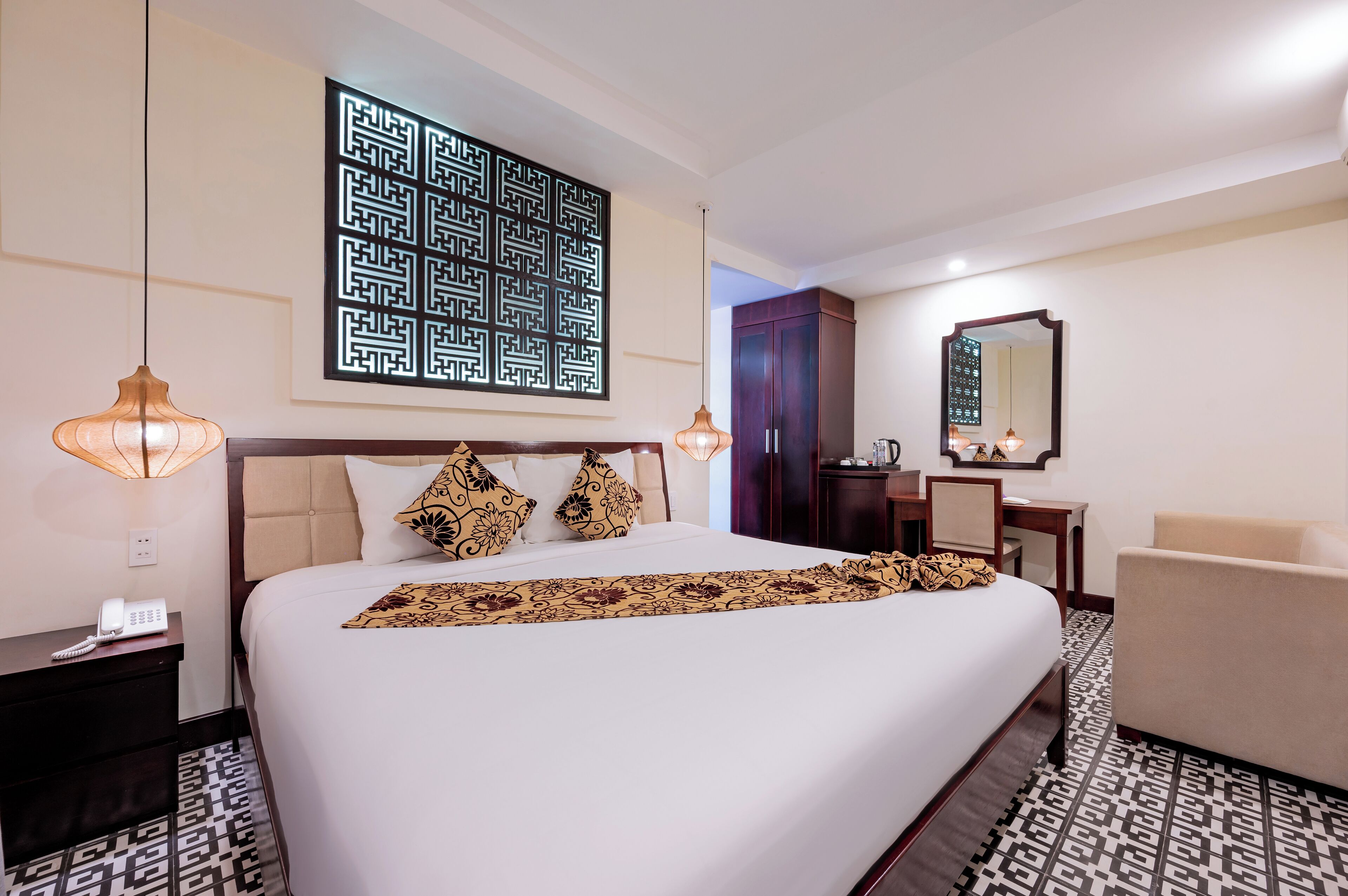 A hotel room with a large bed, bedside lamps, a desk, a chair, a wardrobe, and a decorative wall piece.
