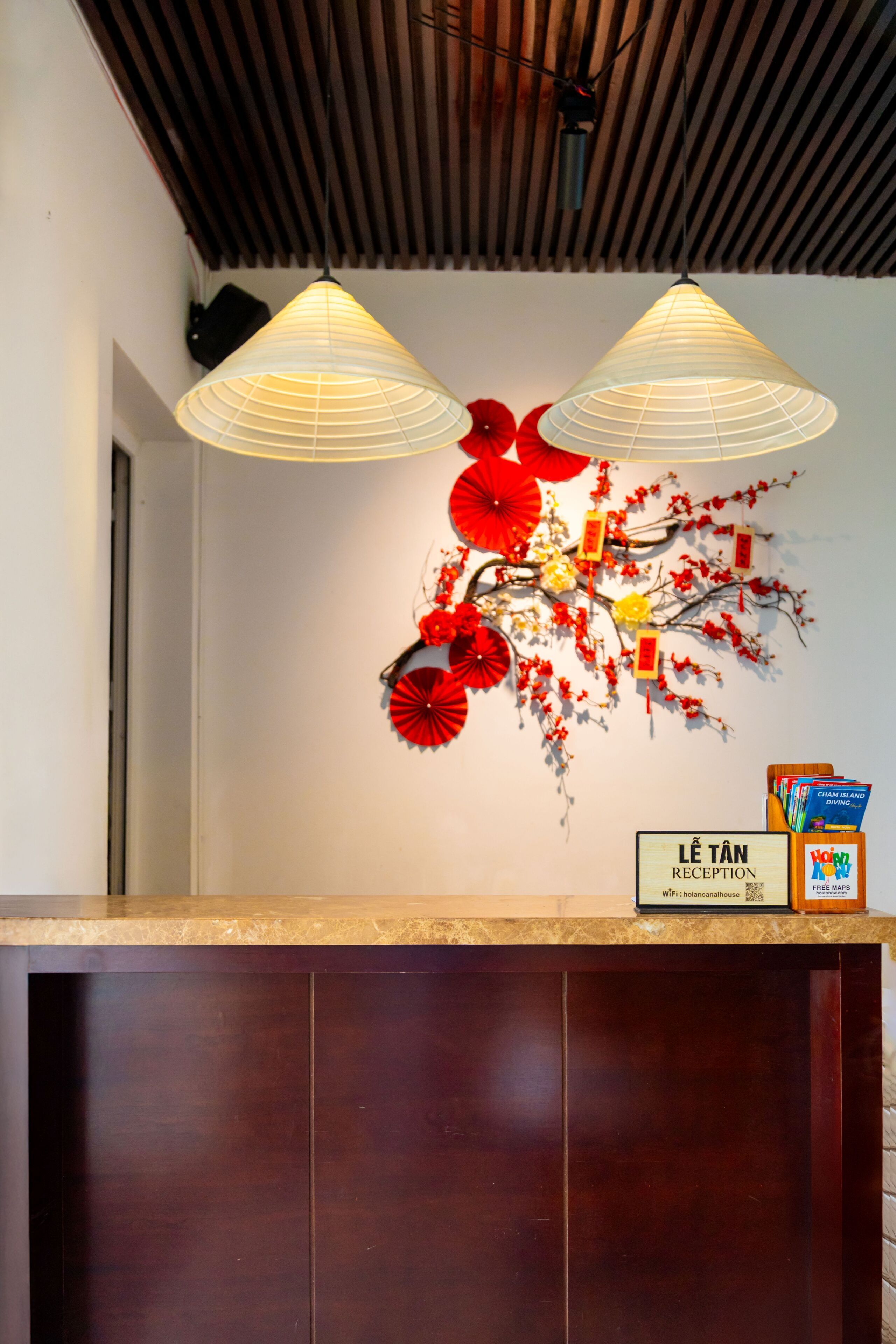 Zona de recepción con un mostrador de madera, dos lámparas colgantes y una decoración de pared con elementos rojos y amarillos.