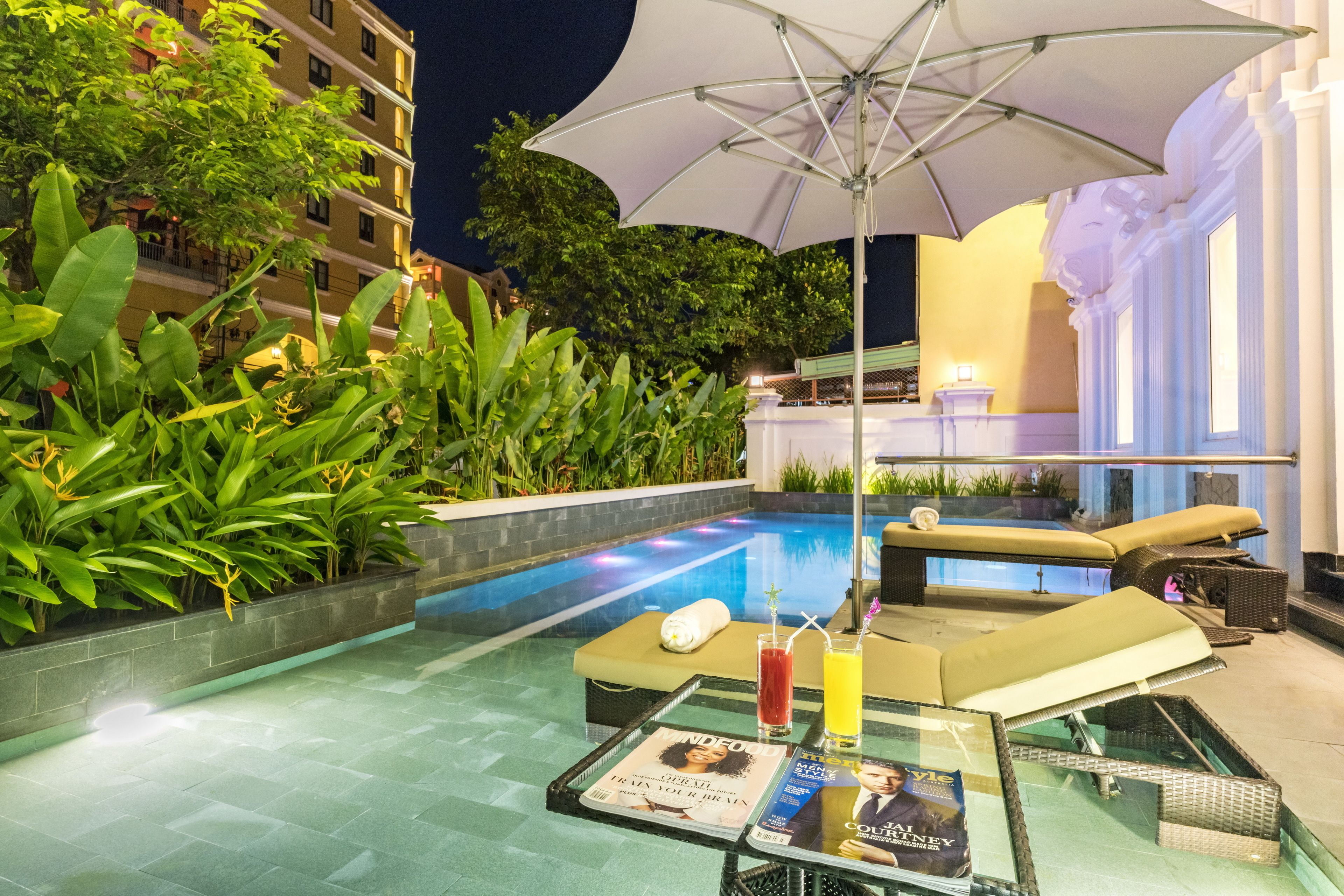 Zona de piscina con sillas de descanso, una mesa con bebidas y una revista.