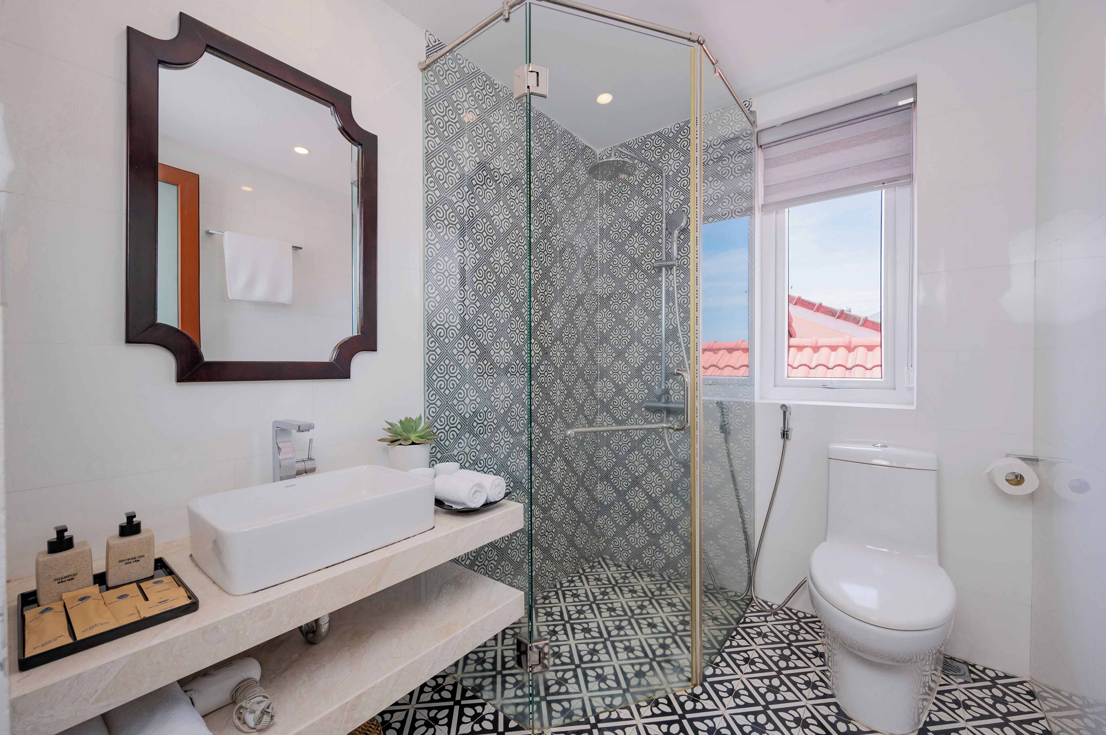 A bathroom with a glass-enclosed shower, a white sink, a toilet, and patterned tiles.