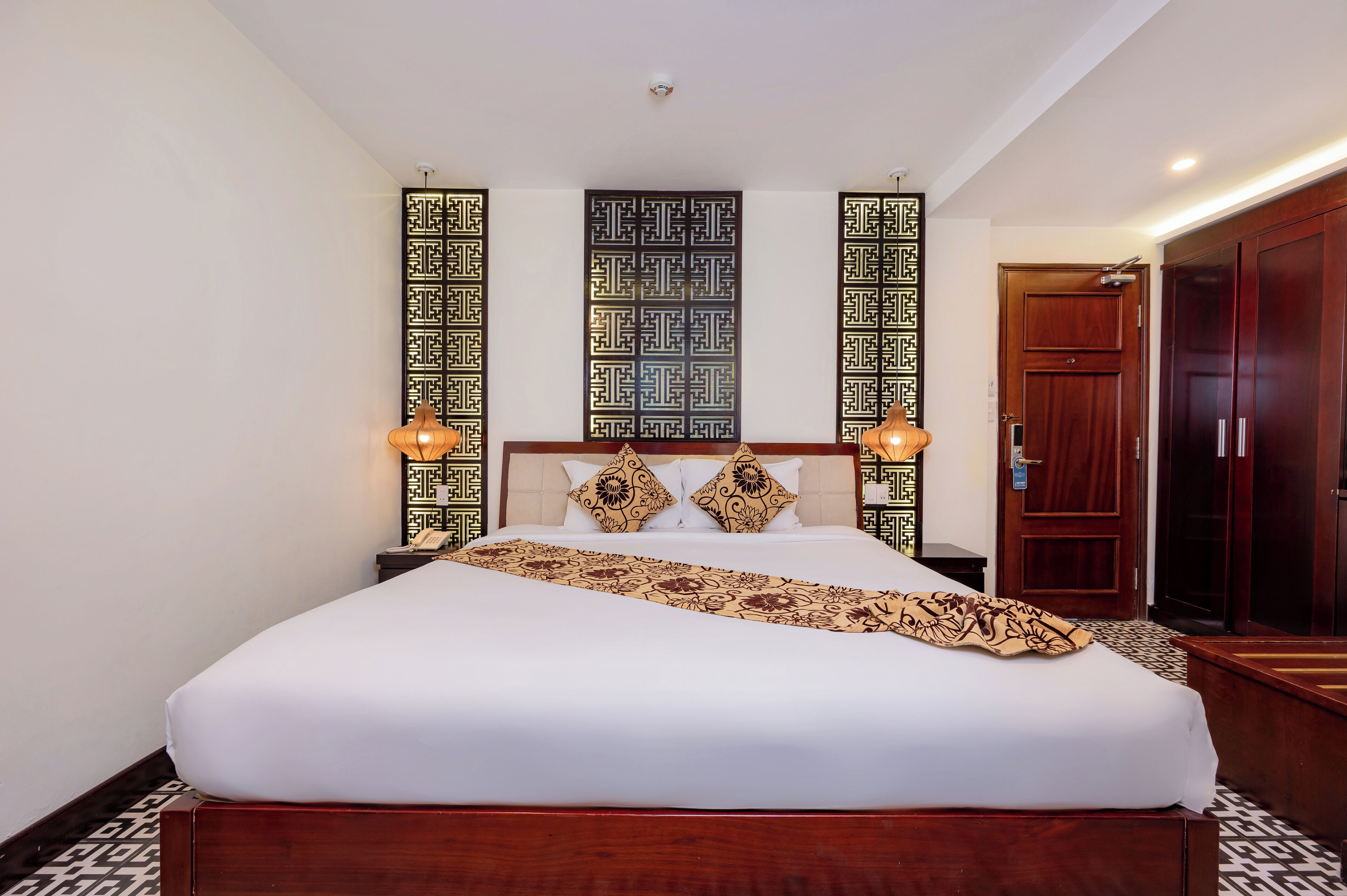 A neatly made bed with a patterned throw, a headboard with decorative panels, and a bedside table with a lamp.