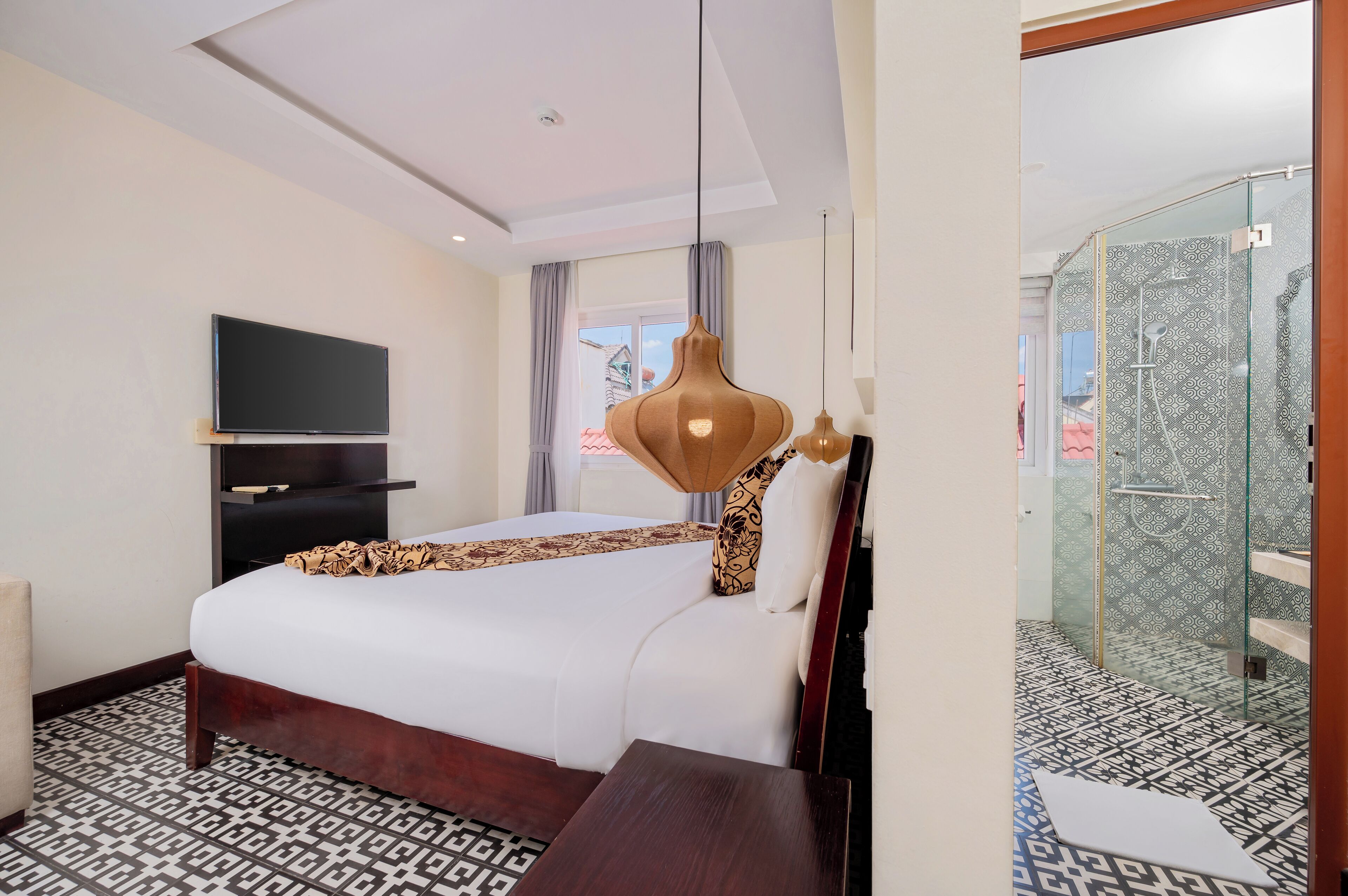 A hotel room with a bed, a TV, a shower, and patterned flooring.
