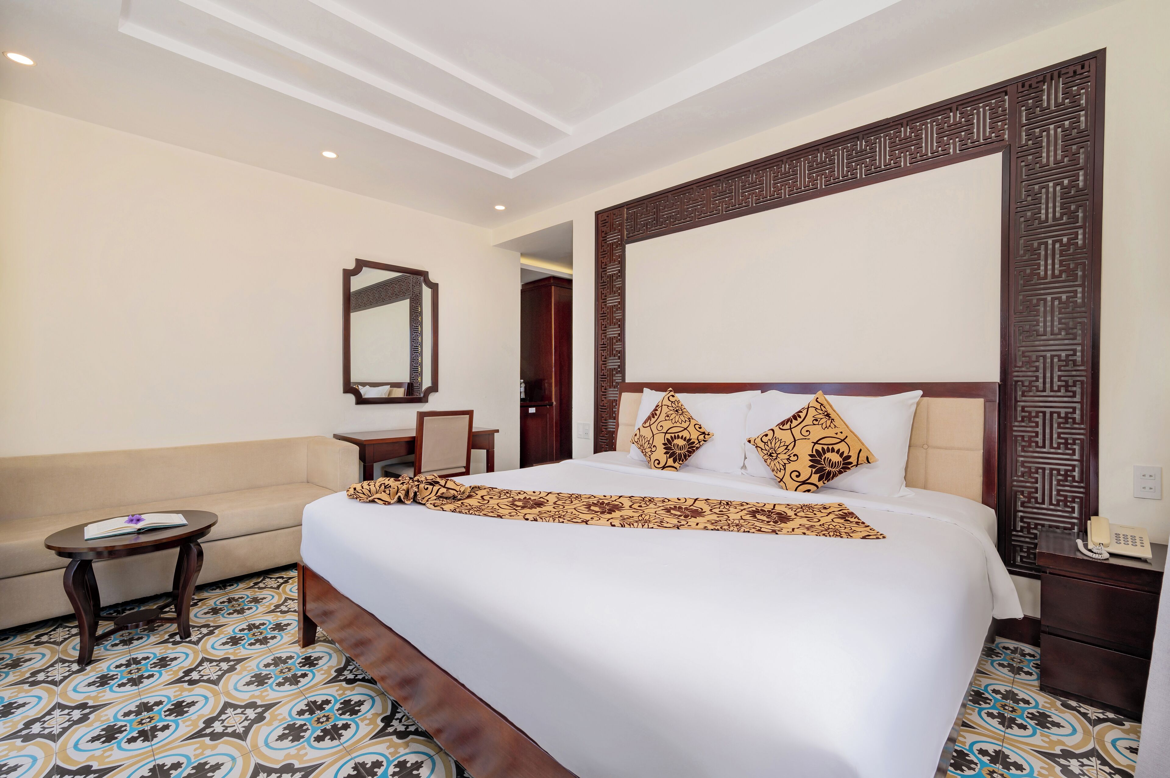 Une chambre d’hôtel avec un grand lit, un canapé, une petite table, un miroir et un sol à motifs.