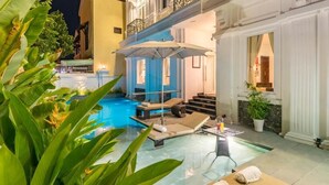 A pool area with lounge chairs and a table, surrounded by plants and a staircase leading to an upper level. - Hoi An Canal House Riverside By Haviland (Da Nang)
