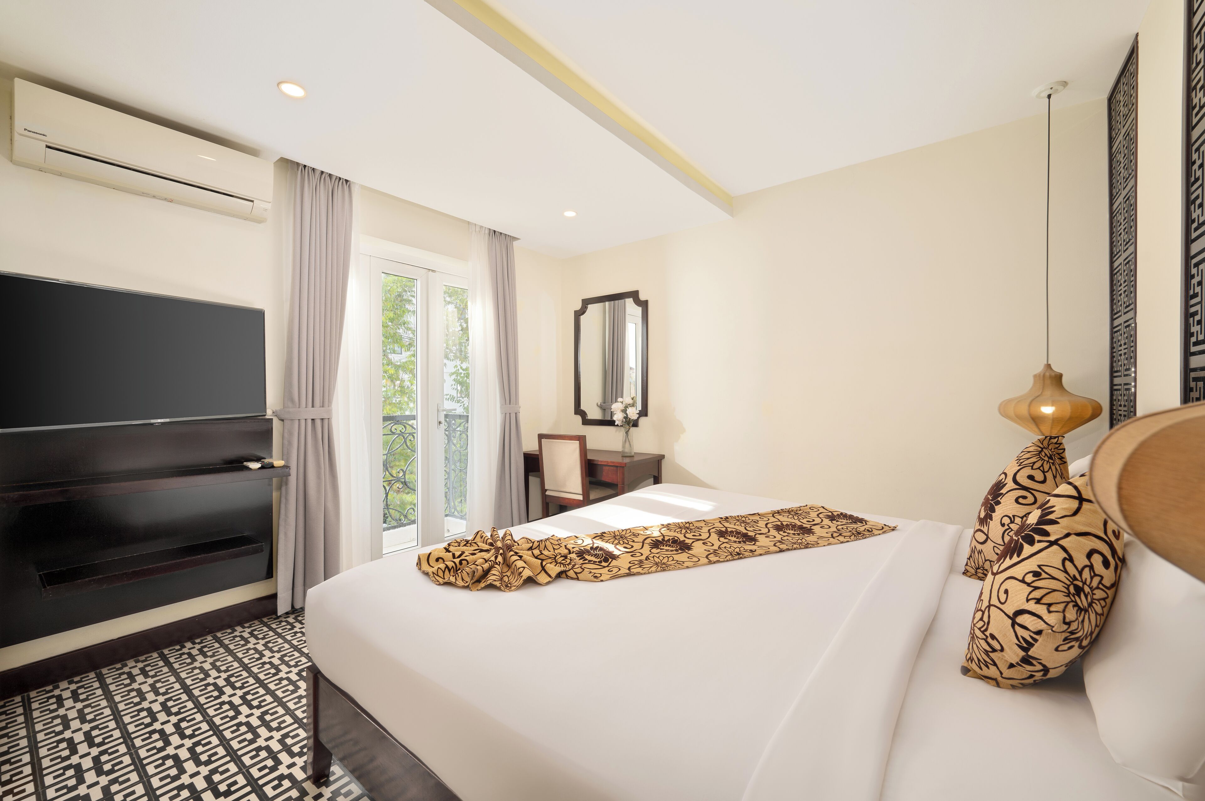 A hotel room with a large bed, a TV, a desk, and a balcony with curtains.